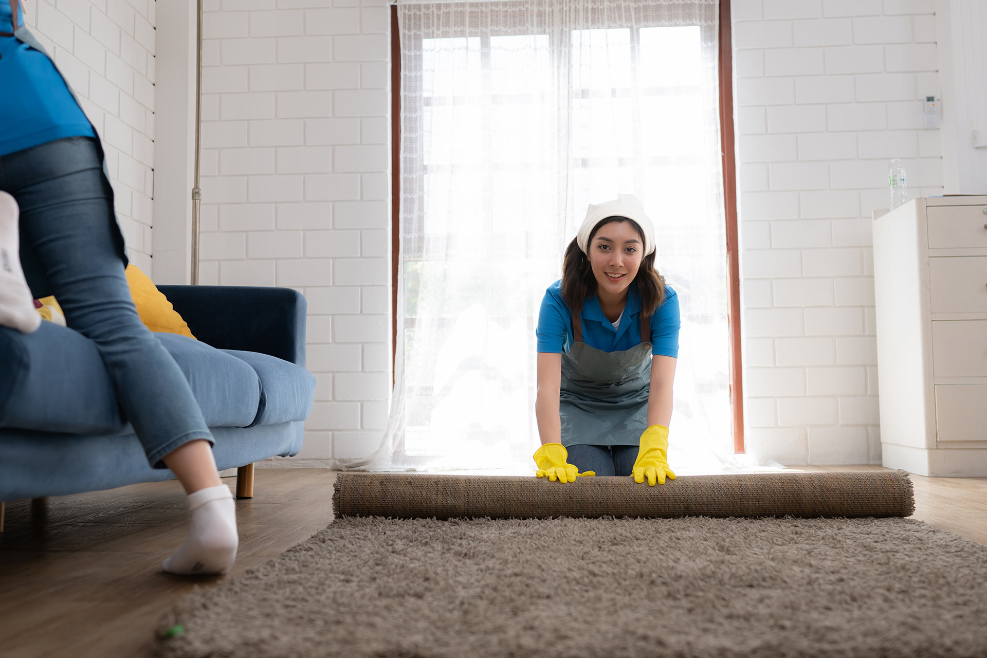 A woman is rolling a rug in a living room.