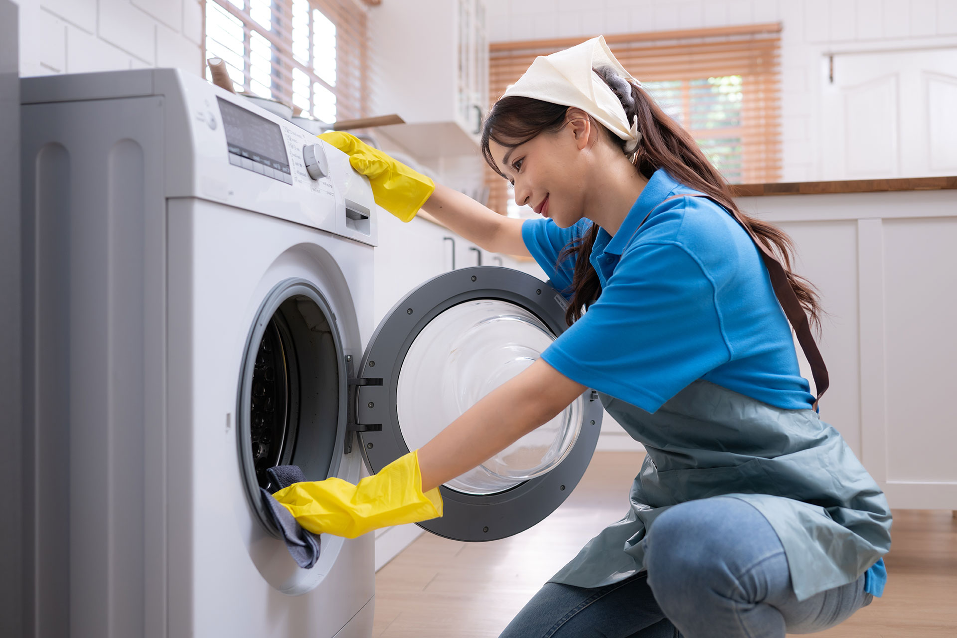 A woman is cleaning a washing machine in a kitchen.
