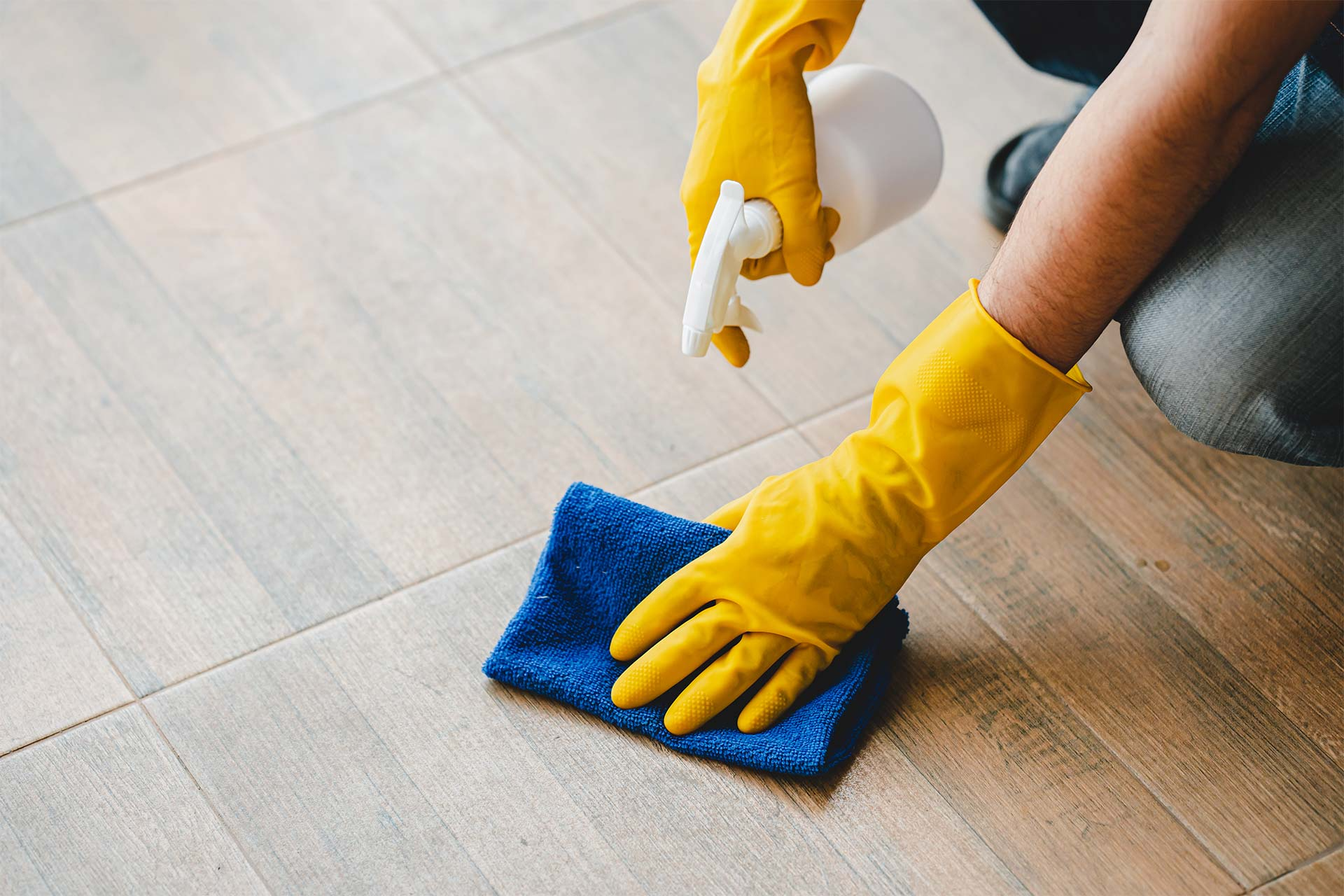 A person wearing yellow gloves is cleaning the floor with a cloth and spray bottle.