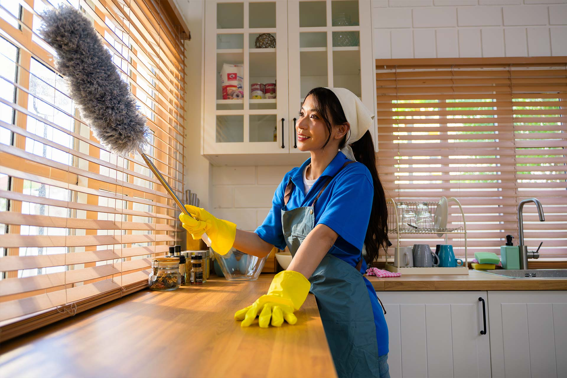 A woman is cleaning a kitchen counter with a duster.
