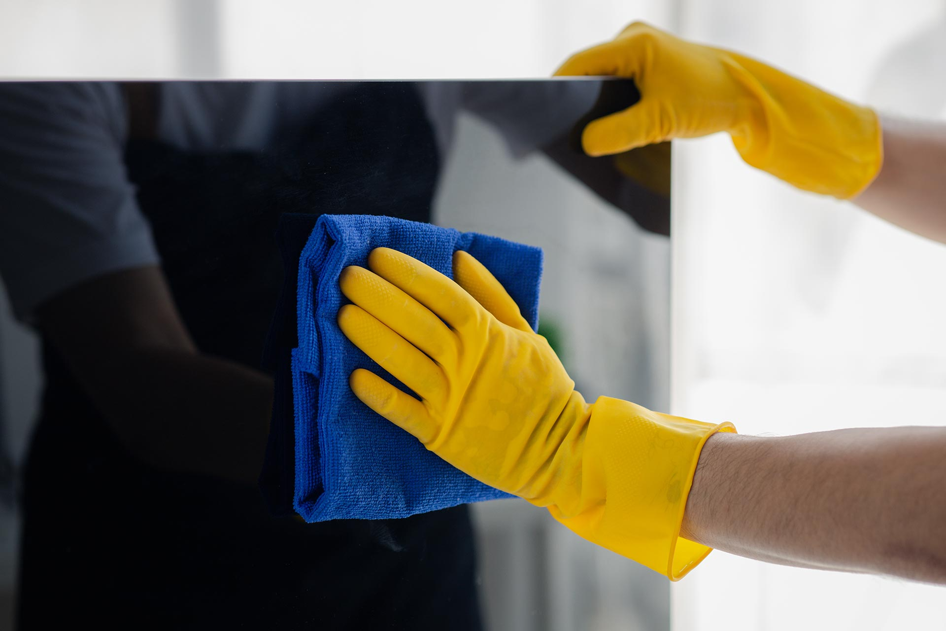 A person wearing yellow gloves is cleaning a tv screen with a blue cloth.