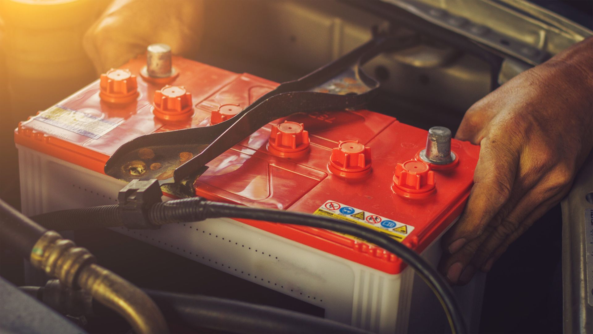 Two car batteries in an engine bay, with a hand adjusting a cable.