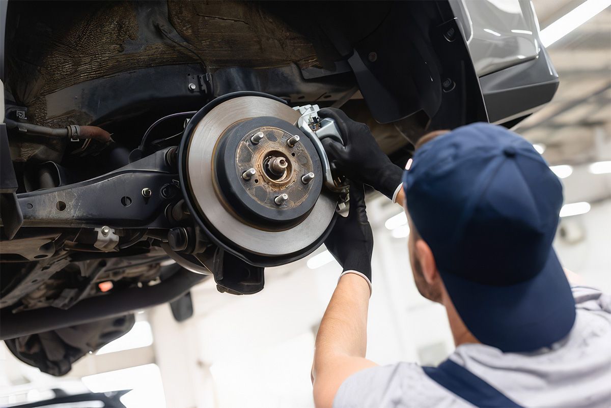 Mechanic inspecting a car’s exposed wheel brake assembly with a wrench in a garage