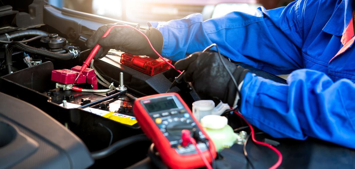 Mechanic testing a car battery with a red multimeter under the hood
