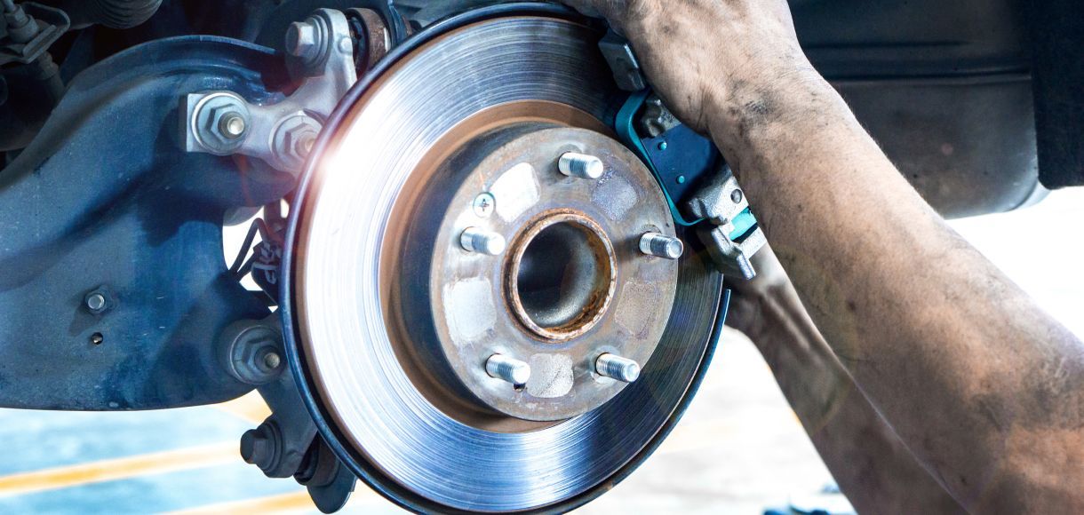 Mechanic tightening a car brake rotor with a wrench under the vehicle
