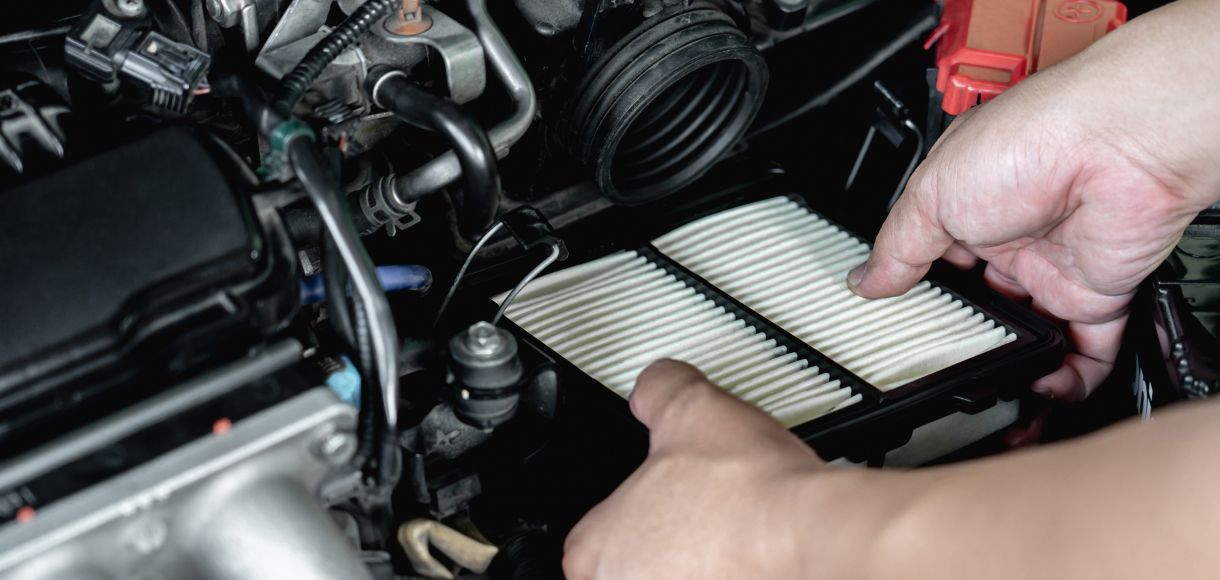 Hands replacing a white air filter in a car engine bay