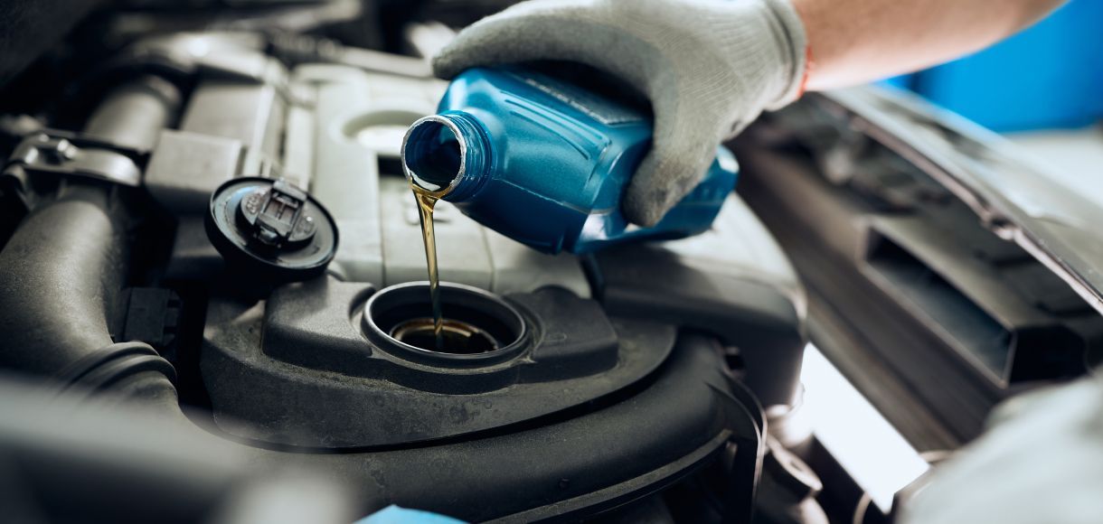 A gloved hand pours blue motor oil into a car engine