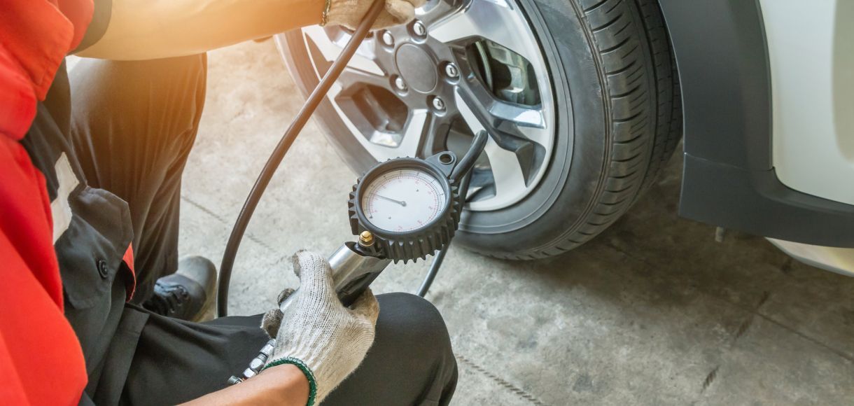 Mechanic checking tire pressure on a car wheel with a gauge in a garage