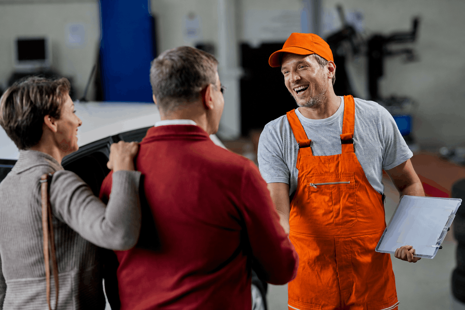 Worker in orange overalls talking with two people indoors, holding papers and smiling