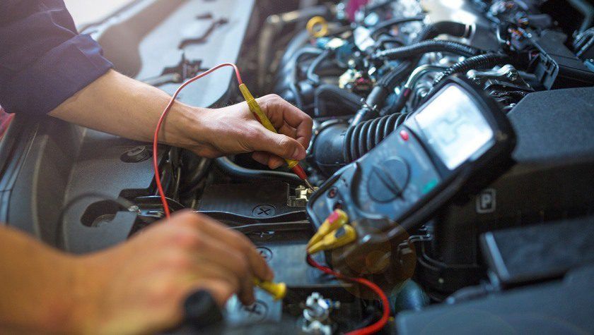 Mechanic testing car wiring with probes under the hood, laptop nearby