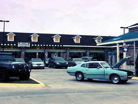 Classic cars parked outside a strip mall storefront on a sunny day