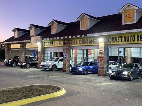 Auto repair strip mall at dusk with parked cars and signs for oil changes and complete auto repair