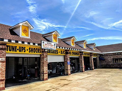 Auto repair shop exterior with brick bays and signs for tune-ups, shocks, brakes, AC, and alignment under a blue sky