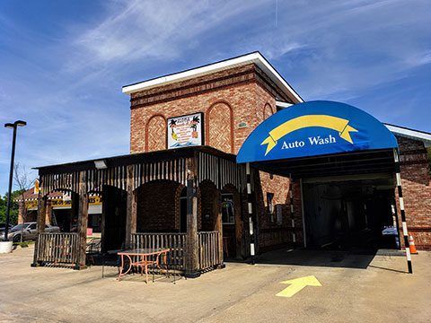 Brick auto wash building with blue awning and yellow arrow at the entrance