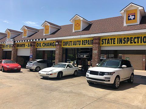 Auto service strip mall with oil change, repair, and state inspection signs; cars parked outside.