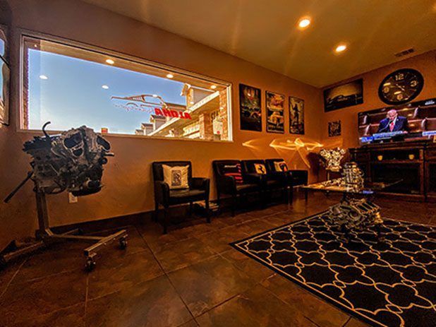 Warm waiting room with dark tile floor, chairs, wall art, a TV, and a large window.