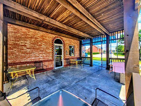 Covered brick patio with concrete floor, wooden ceiling beams, benches, and a view of a grassy yard through open sides