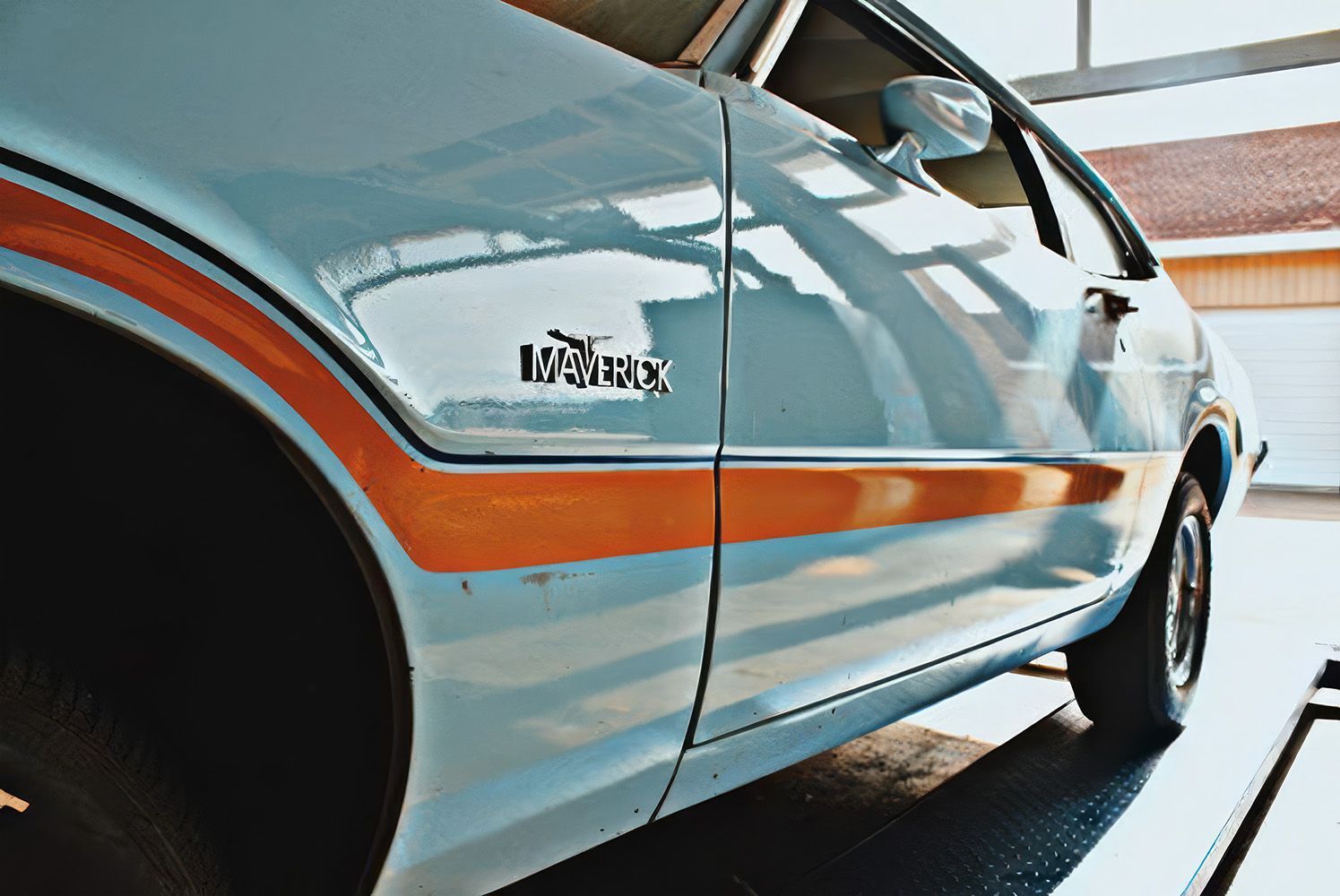 Light blue classic car with orange stripe viewed from the side in a garage