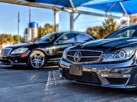 Two black Mercedes sedans parked under a canopy in a sunny lot