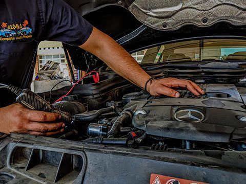 Mechanic working under an open car hood, using tools on the engine bay.