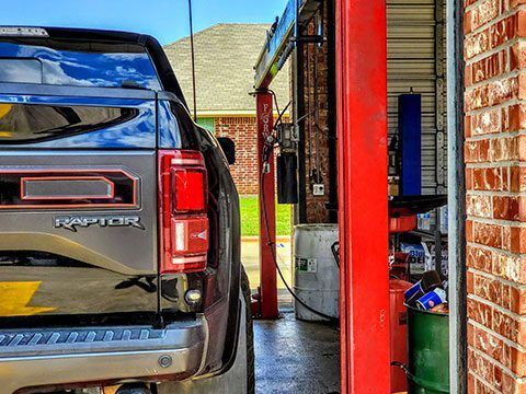 Black pickup truck parked in a narrow driveway beside a red metal post and brick wall.
