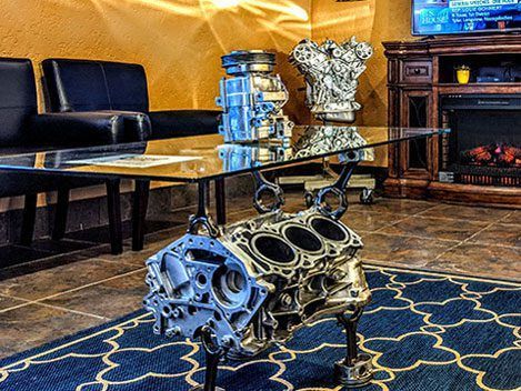 Automobile engine block on a glass table in a stylish living room with dark furniture and patterned rug