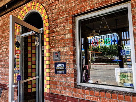 Brick storefront with arched doorway and window, featuring a colorful neon sign inside