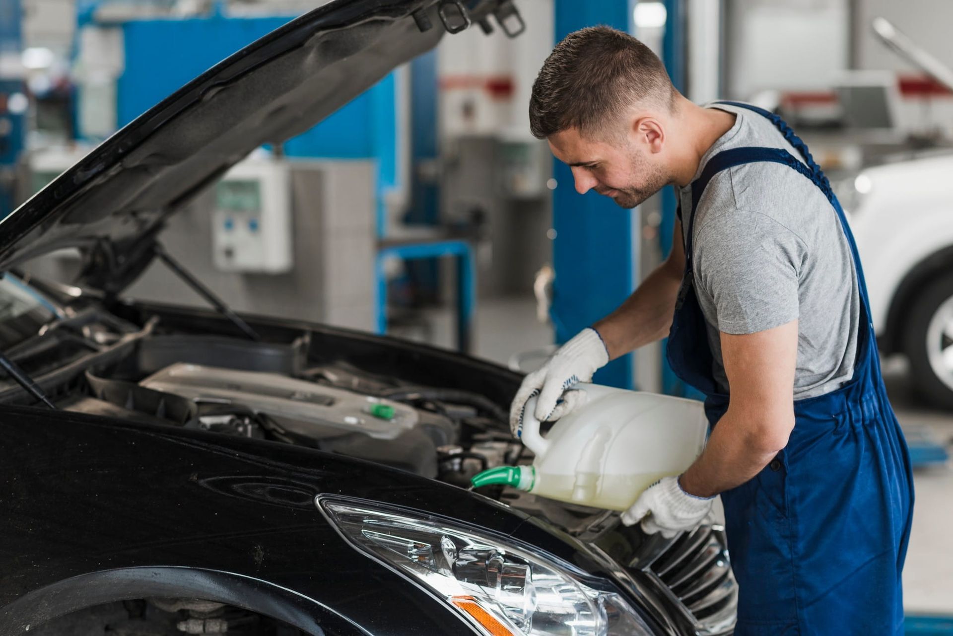 Mechanic in blue overalls checking a black carβs engine in an auto repair shop