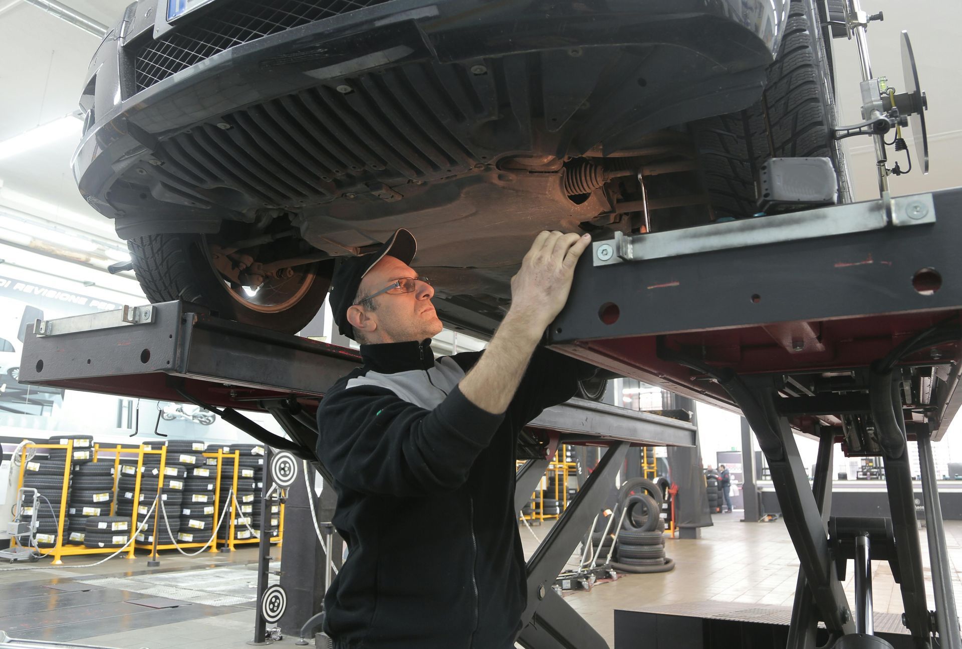 Mechanic inspecting the underside of a car on a lift in an auto shop