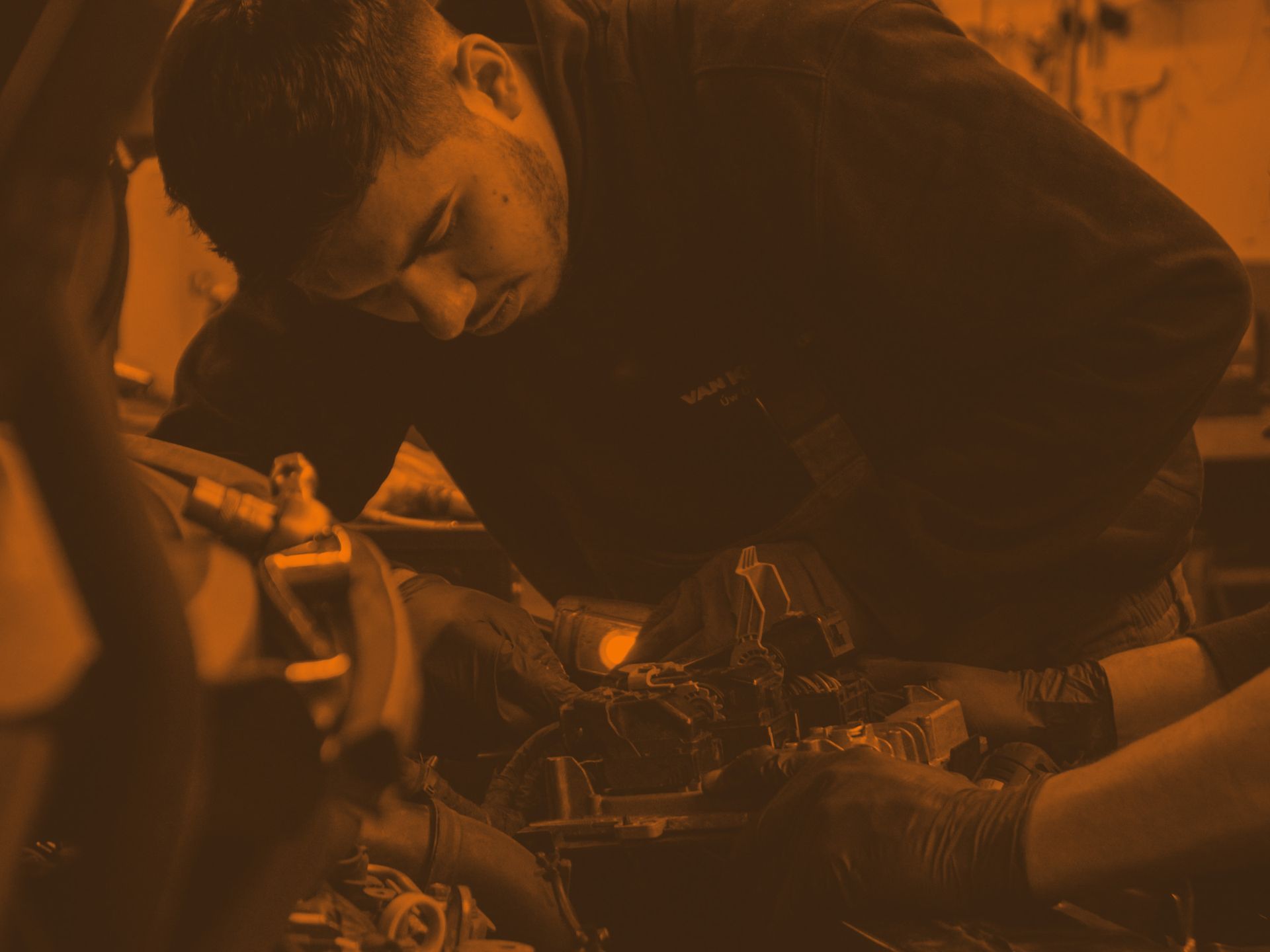 Mechanic working under a car hood, inspecting engine components in warm orange light