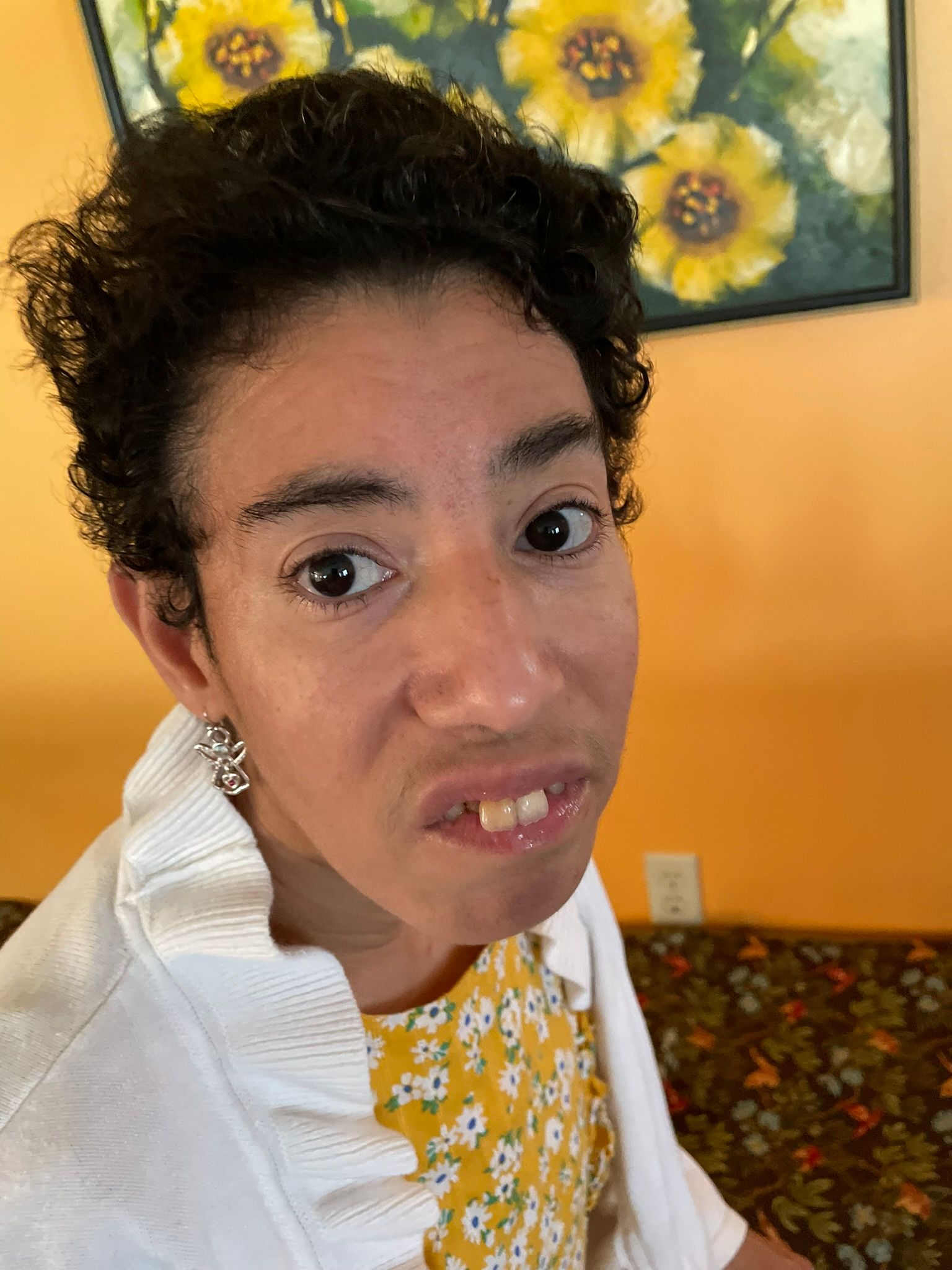 A woman is making a funny face in front of a painting of flowers.