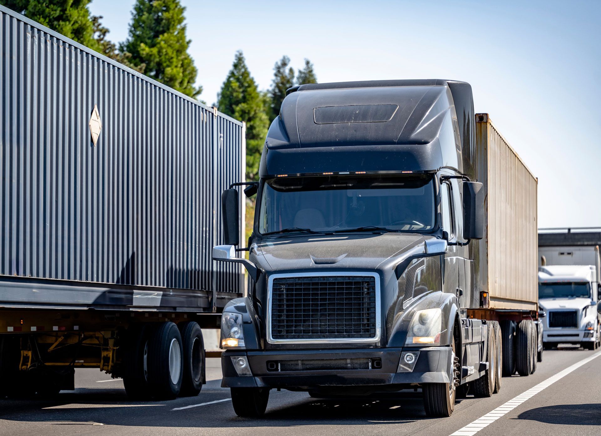 Semi truck driving on a highway beside other trucks and shipping containers