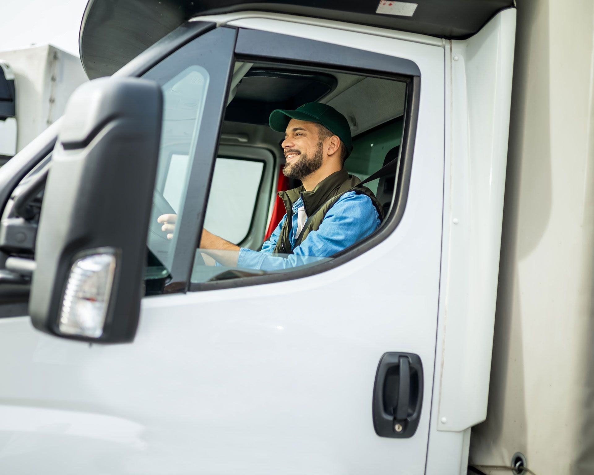 Man driving a white truck, seen through the open driver’s window.