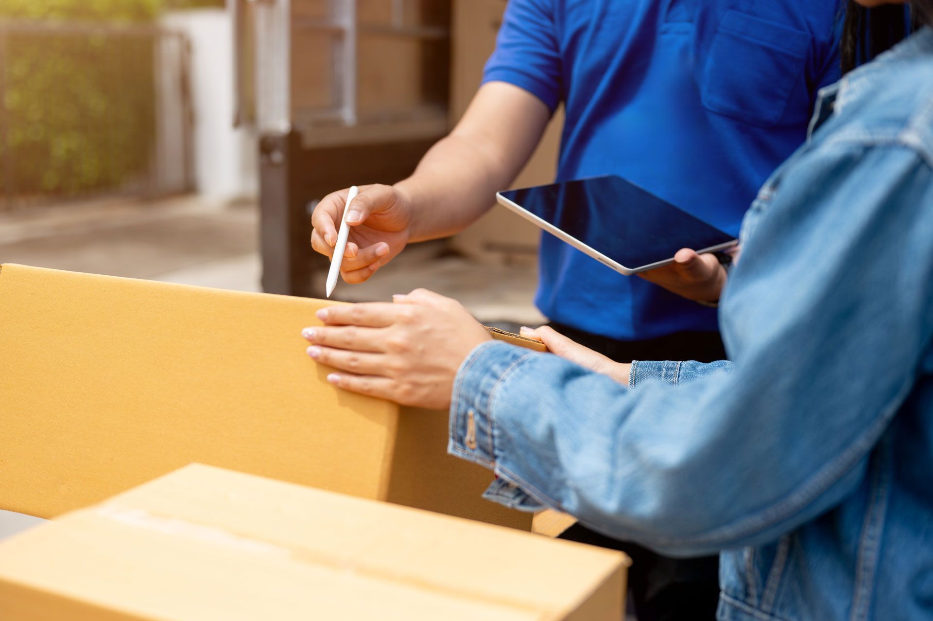 Two people packing a cardboard box outdoors, one holding a pen and clipboard.