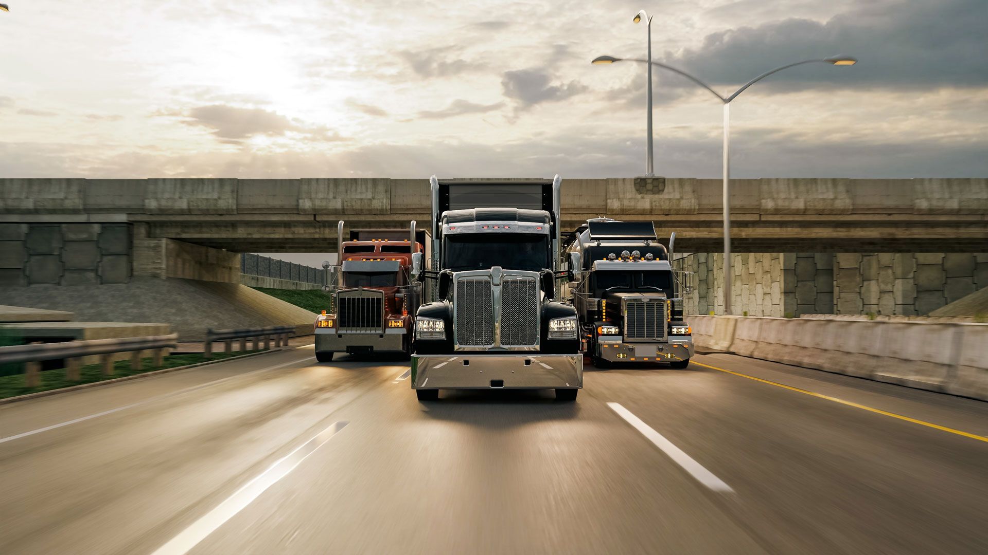 Three semi trucks driving side by side on a wet highway under an overpass at dusk