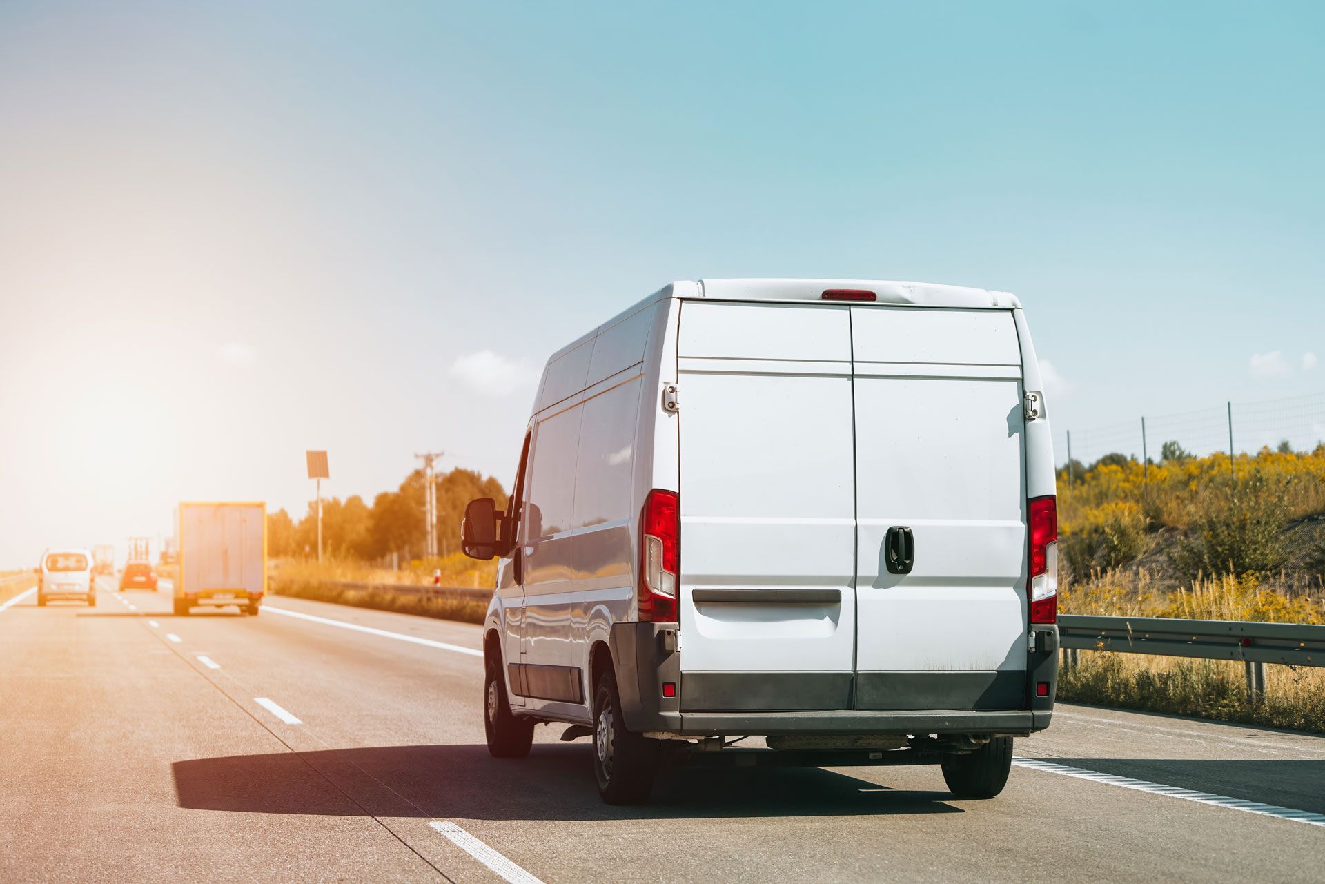 White delivery van driving on a sunny highway with traffic ahead
