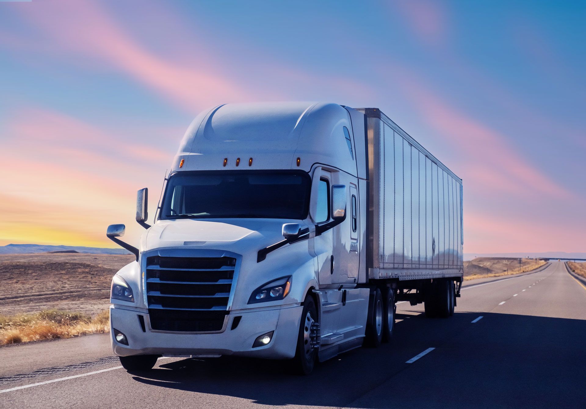 White semi-truck driving on a highway at sunset with pink sky and open desert roadside