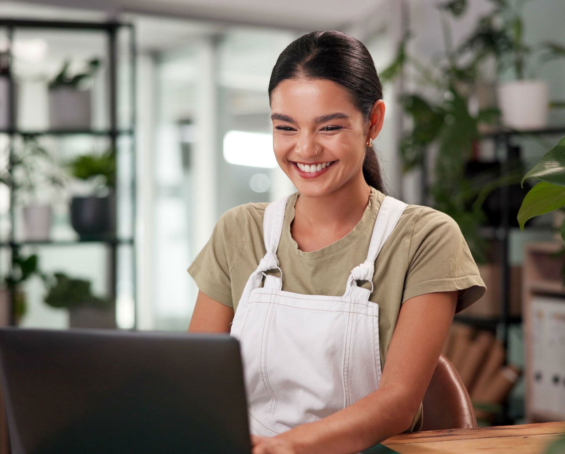 Smiling woman in apron using a laptop in a bright café or kitchen workspace
