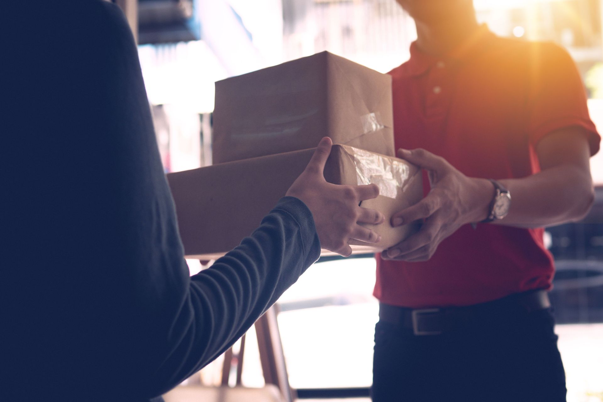 Two people pass a cardboard box between them in a sunlit doorway.