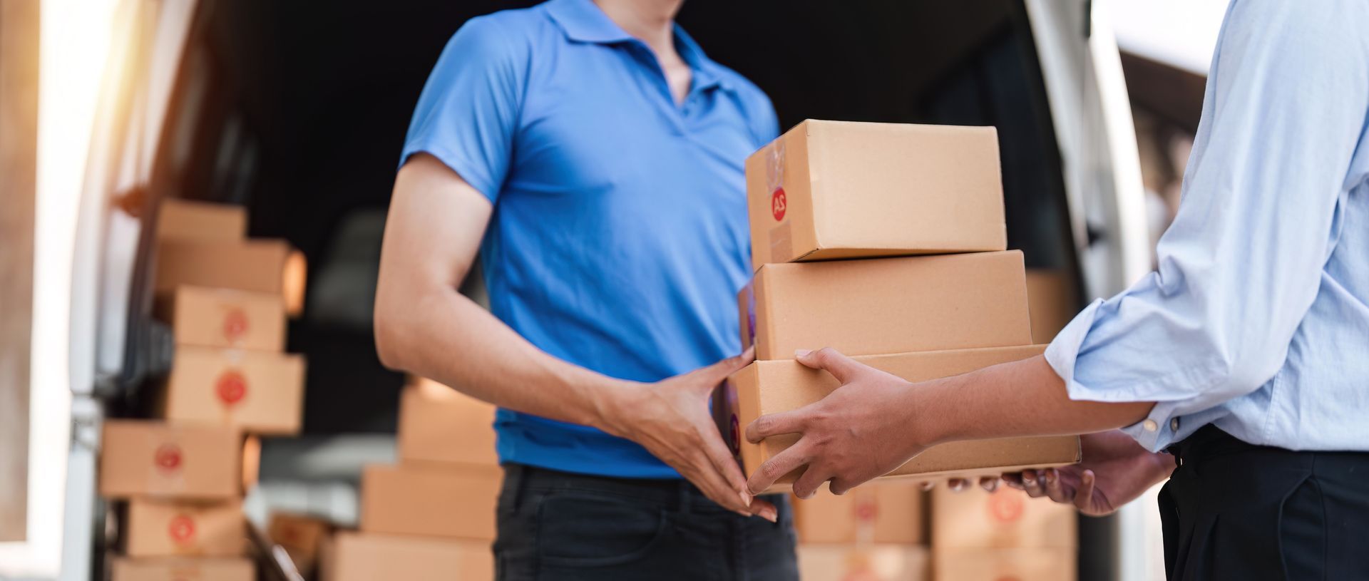 Two people passing cardboard boxes in a warehouse, with more stacked boxes in the background