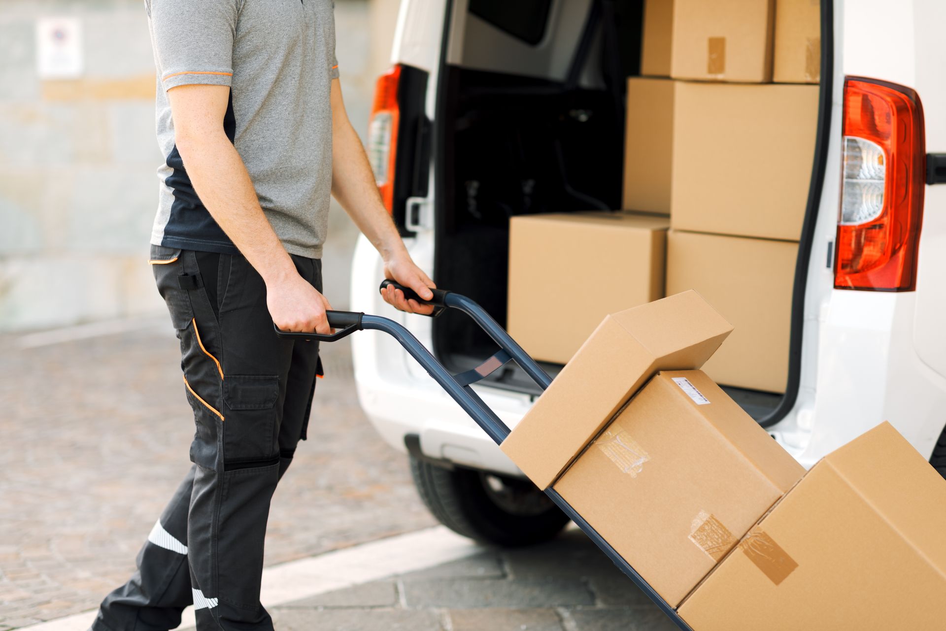Person unloading cardboard boxes from a white van with a hand truck