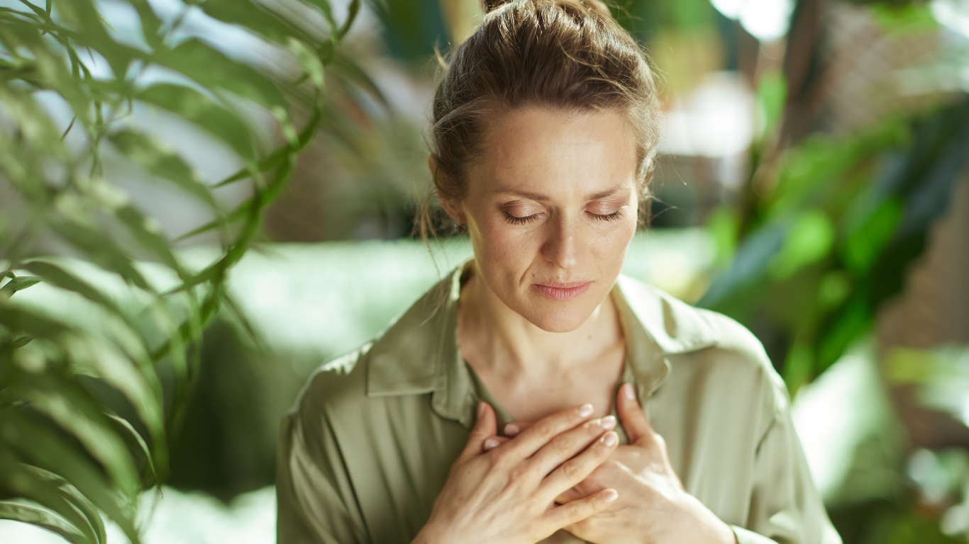 Woman with eyes closed, hands on chest, meditating in a green indoor setting