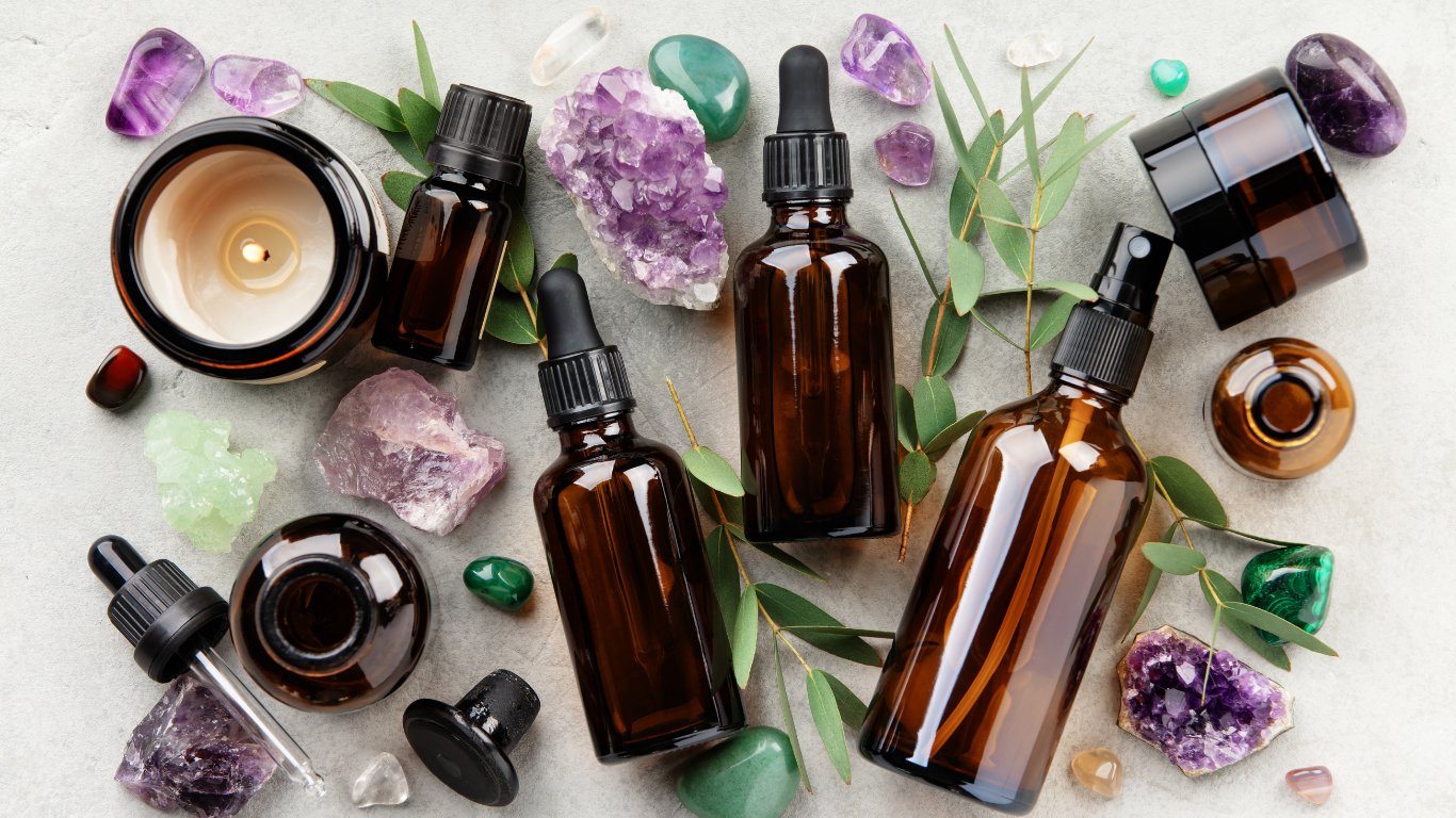 Amber glass essential oil bottles with droppers, crystals, and green leaves arranged on a white surface