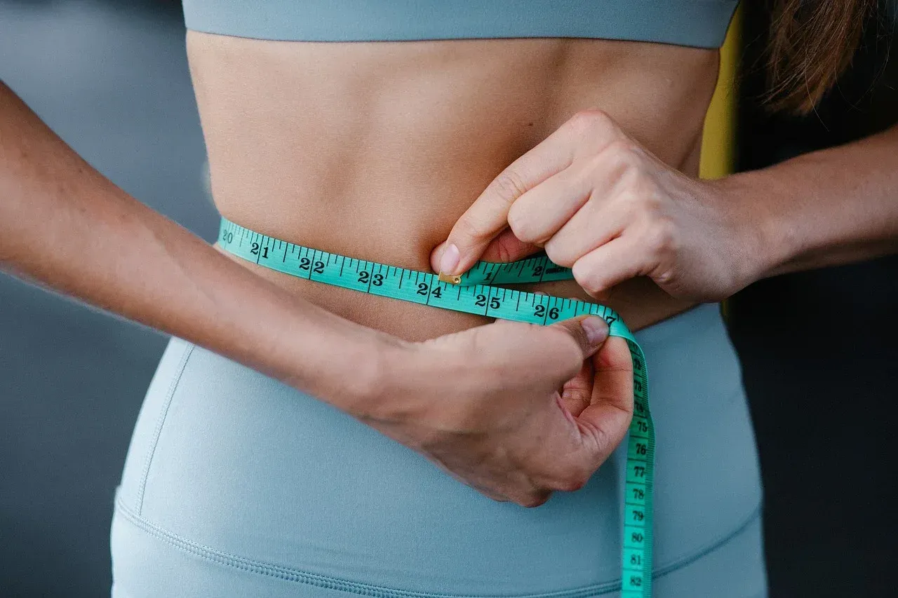 Hands measuring a waist with a turquoise tape measure, showing body measurements