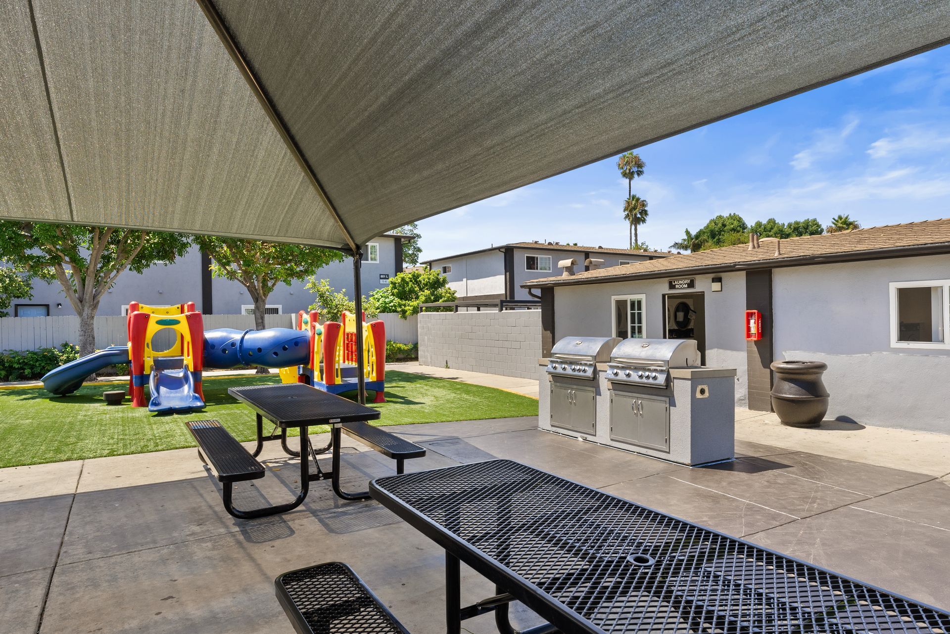 Two picnic tables next to two BBQ grills and small playground 