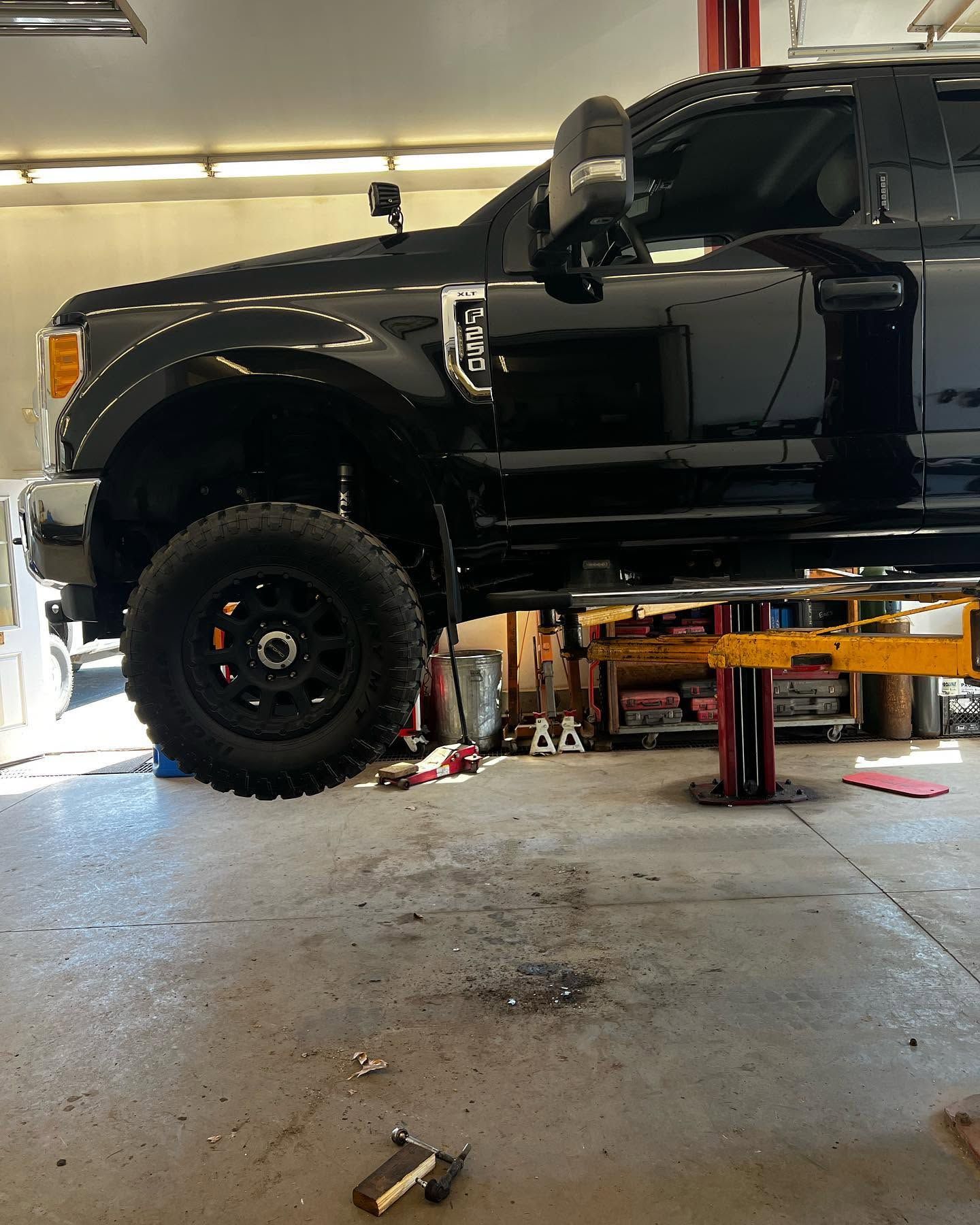 Black lifted pickup truck on a garage lift, viewed side-on inside an auto shop | Cota's Auto Repair