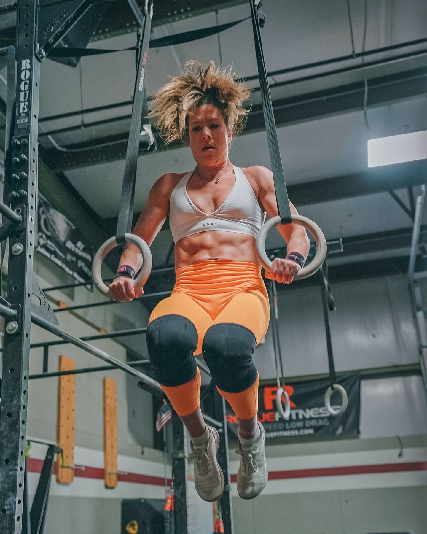 A woman is hanging from gymnastic rings in a gym.