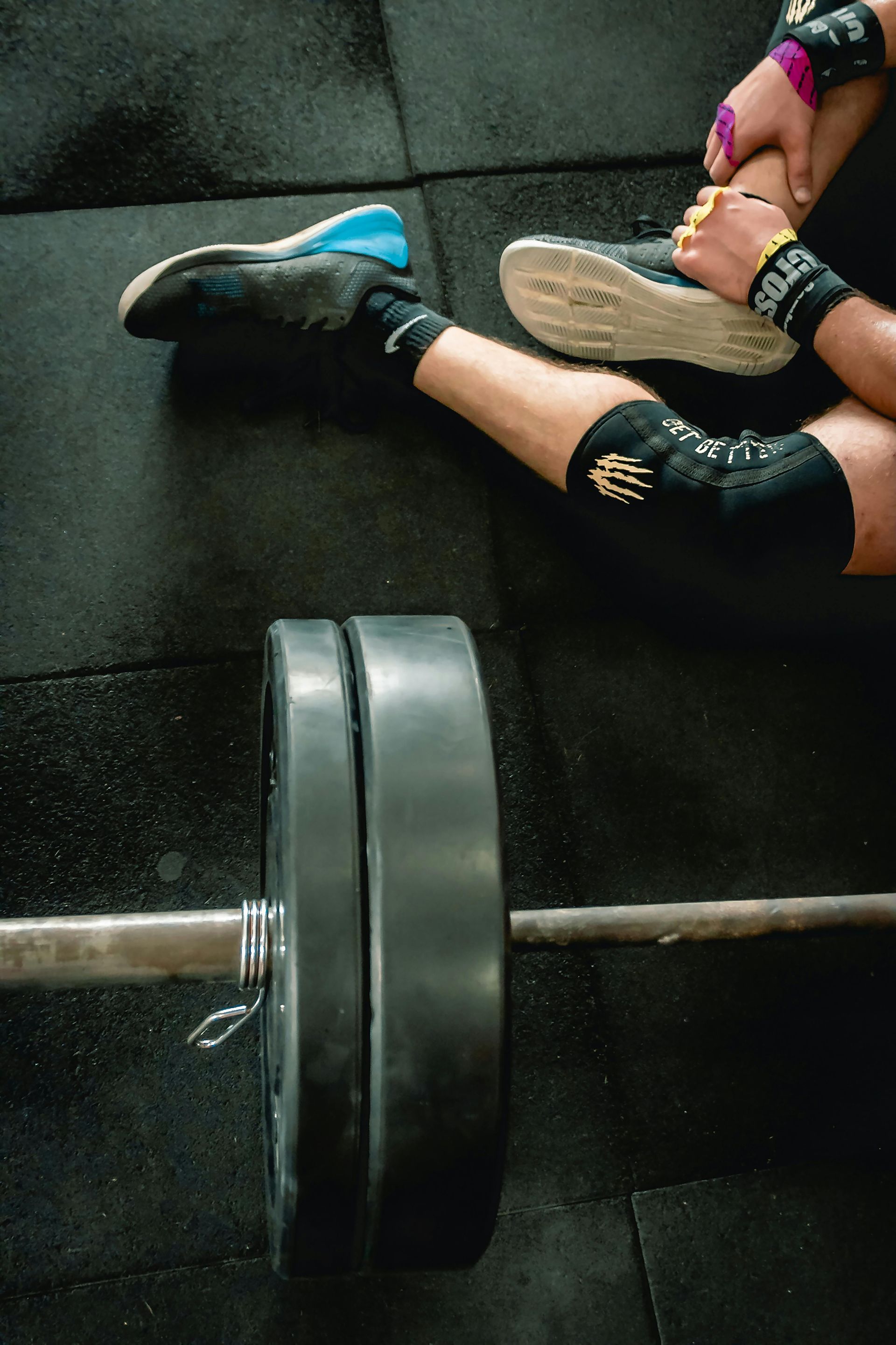 A person is sitting on the floor next to a barbell in a gym.