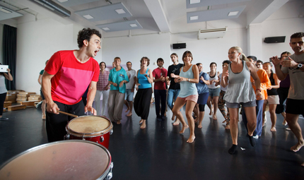 Um grupo de pessoas está dançando e tocando bateria em uma sala.