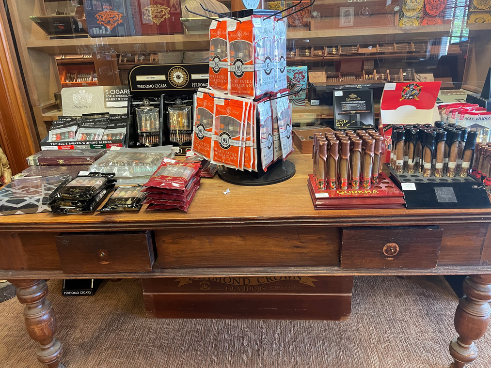 Wooden display table with assorted packaged snacks and orange drink cartons in a shop.